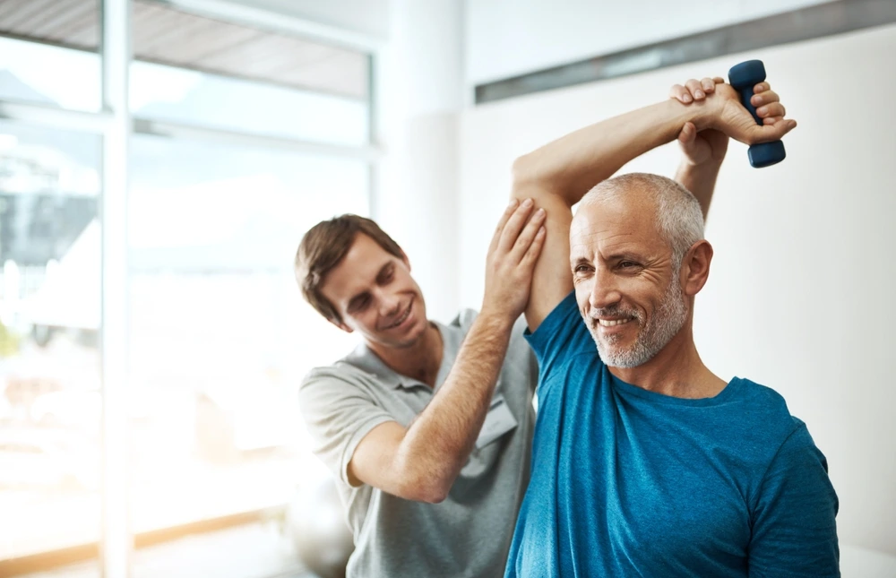 The therapist of Physio Well-th helps a man do a arm exercise
